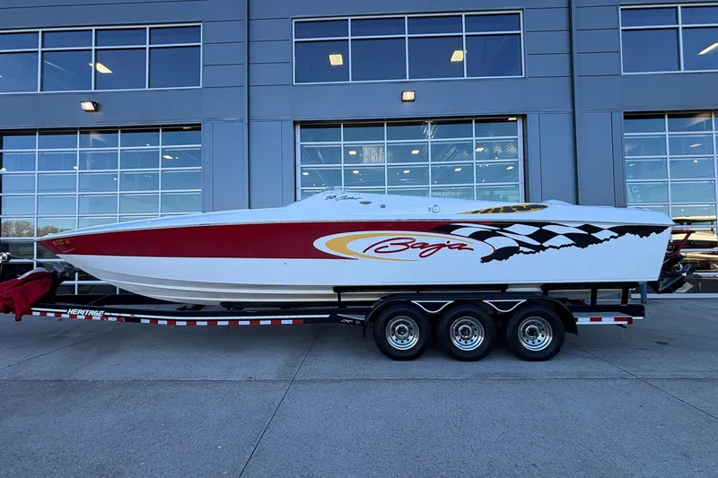 The Image of 2001 Baja 33 Outlaw speedboat on trailer, red and white design, parked outside a building. - 2