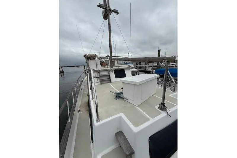 Slide: The Image of 1987 Monk 36 Trawler boat deck with railing and storage box, docked under cloudy skies. - 5