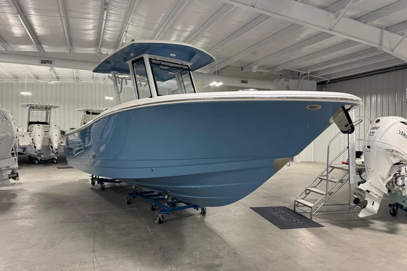 Slide: The Image of 2026 Robalo R270 Center Console boat in showroom, featuring sleek blue design and powerful engine. - 2