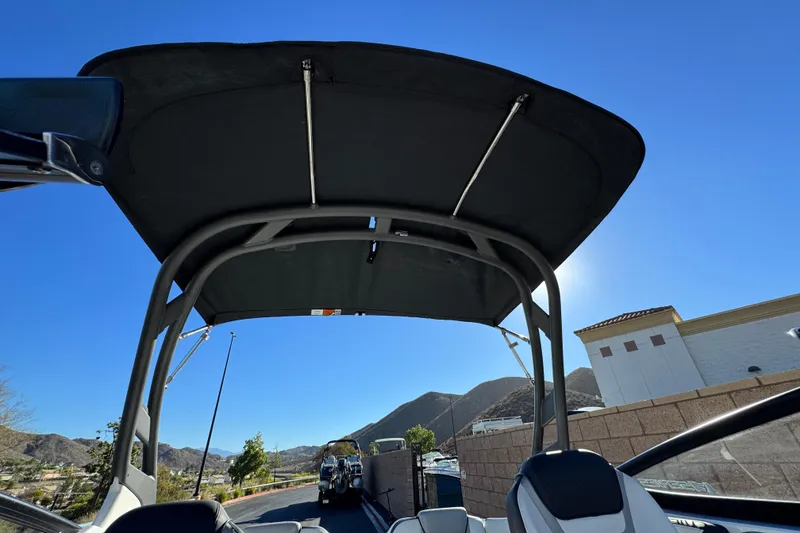 Slide: The Image of 2022 Yamaha Boats 212SE with bimini top, scenic mountain backdrop, clear blue sky. - 10