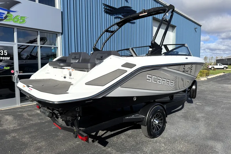 Slide: The Image of 2026 Scarab 210 LX boat on trailer, parked outside showroom, under clear sky. - 4