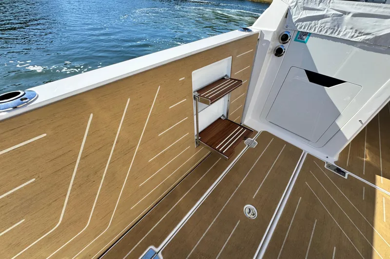 Slide: The Image of 2025 Regal LX43 boat deck with wood finish, featuring storage shelves and water view. - 26