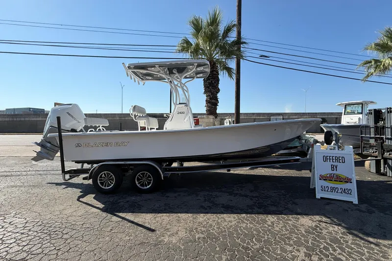The Image of 2026 Blazer Bay 2400 boat on trailer, displayed outdoors with palm trees. - 0