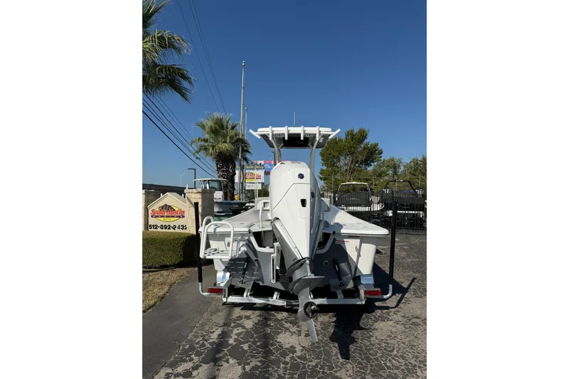 Slide: The Image of 2026 Blazer Bay 2400 boat on trailer, rear view, sunny day, palm trees in background. - 1