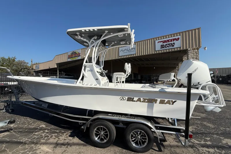 Slide: The Image of 2026 Blazer Bay 2400 boat on trailer outside dealership under clear blue sky. - 2