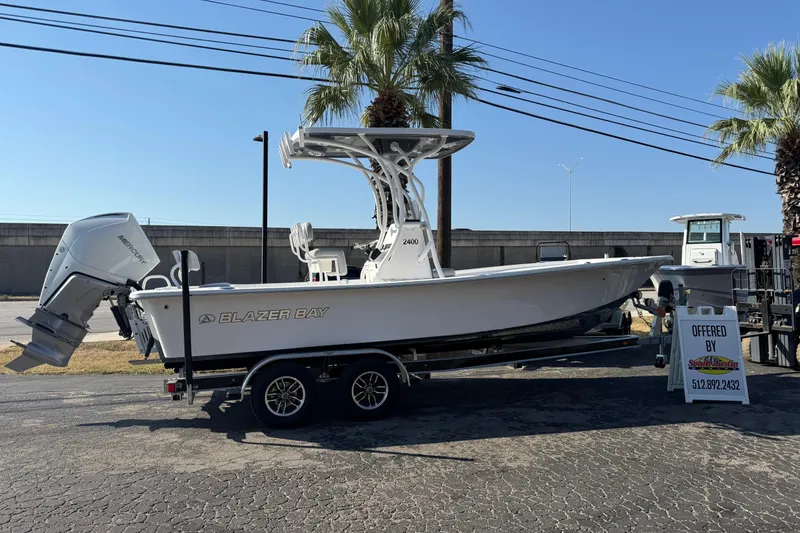 Slide: The Image of 2026 Blazer Bay 2400 boat on trailer, displayed outdoors with palm trees. - 7