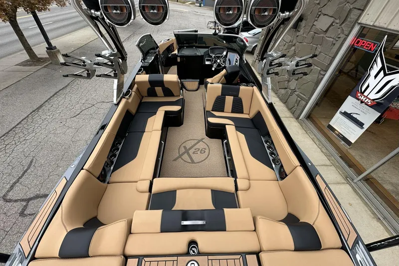 Slide: The Image of 2021 MasterCraft X26 boat interior with tan and black seating, docked near a store. - 12
