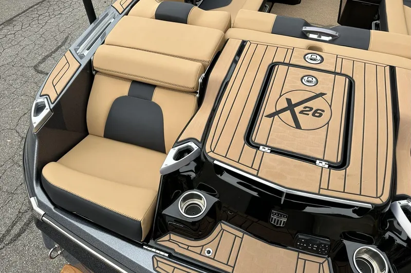 Slide: The Image of 2021 MasterCraft X26 boat interior with tan and black seating, cup holders, and logo detailing. - 14