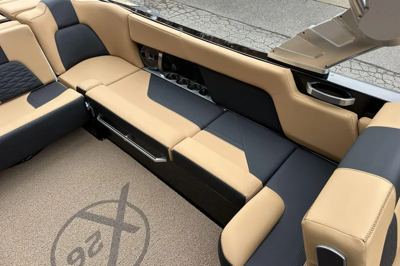 Slide: The Image of 2021 MasterCraft X26 boat interior with tan and black seating, cup holders, and logo carpet. - 8