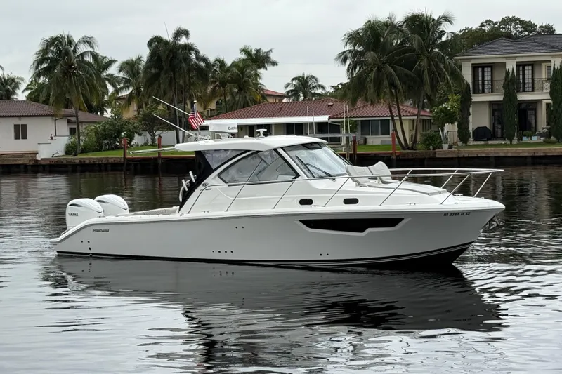 The Image of 2025 Pursuit OS 325 Offshore boat on calm water, surrounded by palm trees and waterfront homes. - 0