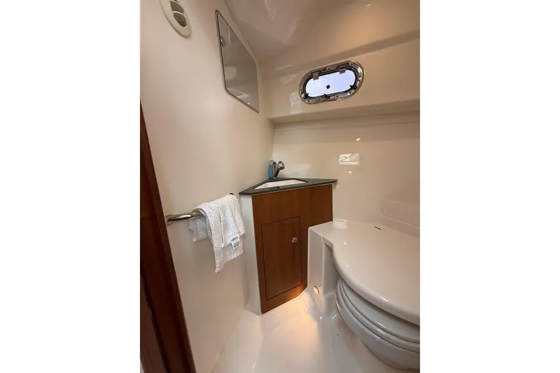 Slide: The Image of 2025 Pursuit OS 325 Offshore boat bathroom with sink, toilet, and porthole window. - 69