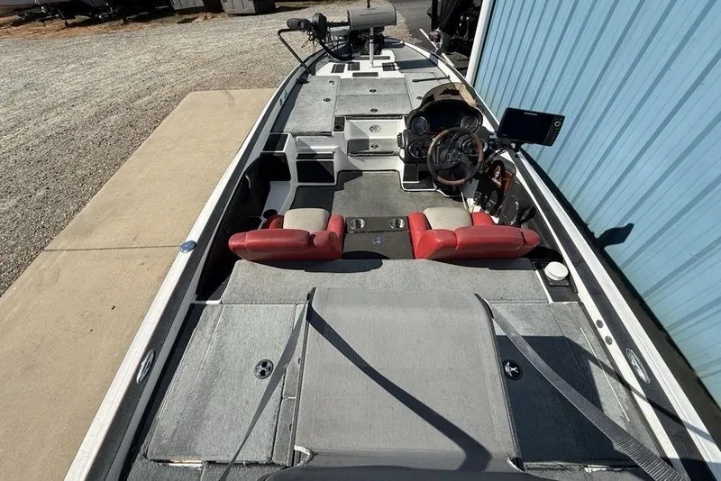 Slide: The Image of 2005 Triton TR-21 boat with red seats and fishing equipment, parked beside a blue building. - 24
