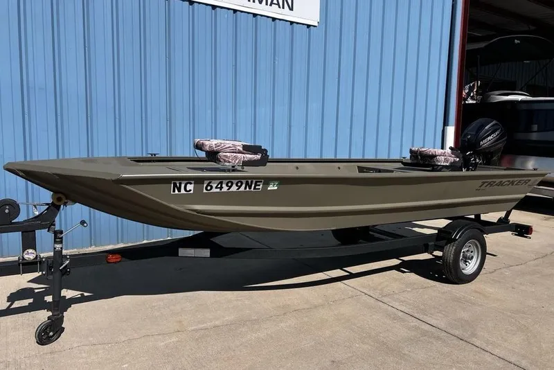 Slide: The Image of 2025 Tracker Grizzly 1648 Utility boat on trailer, parked by blue building. - 3