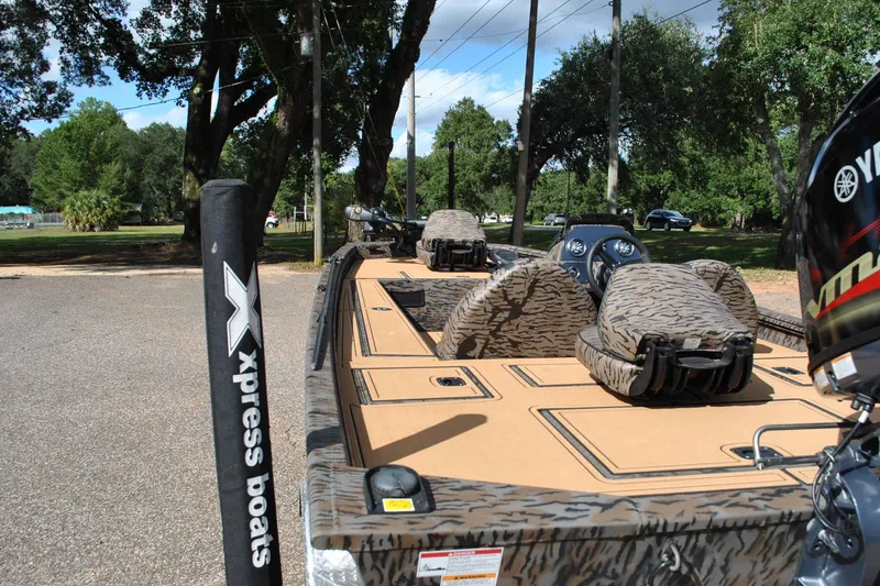Slide: The Image of 2024 Express 180XP boat with camo seats, parked outdoors under trees. - 12