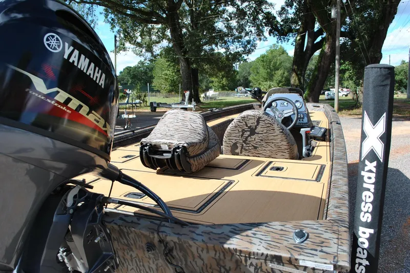 Slide: The Image of 2024 Express 180XP boat with Yamaha engine, camo seats, and Xpress branding in a wooded area. - 13