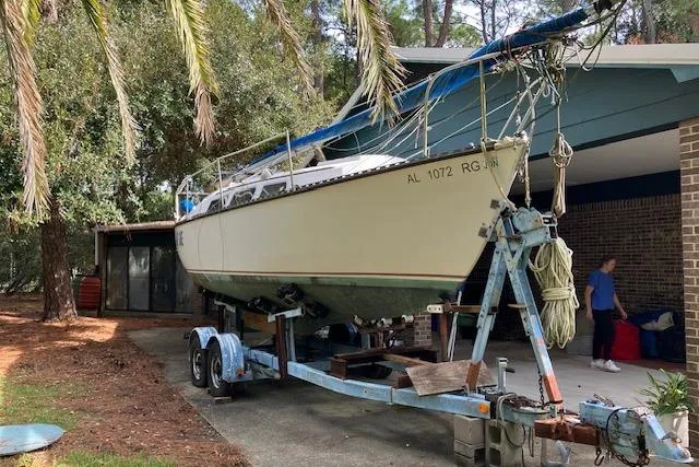 The Image of 1979 Chrysler 26 sailboat on trailer, parked in driveway near trees and house. - 0