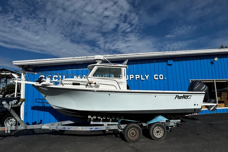 Slide: The Image of 2021 Parker 2320 Sport Cabin boat on trailer, parked outside blue building. - 2