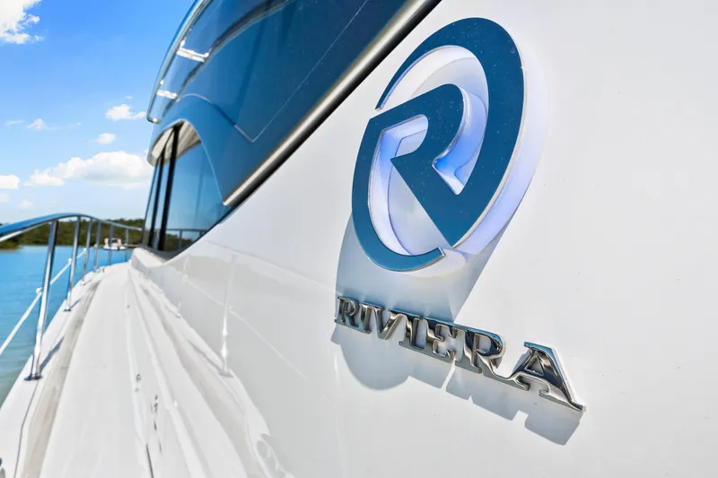 Slide: The Image of 2022 Riviera 5400 Sport Yacht logo on sleek white exterior, sunny day. - 47