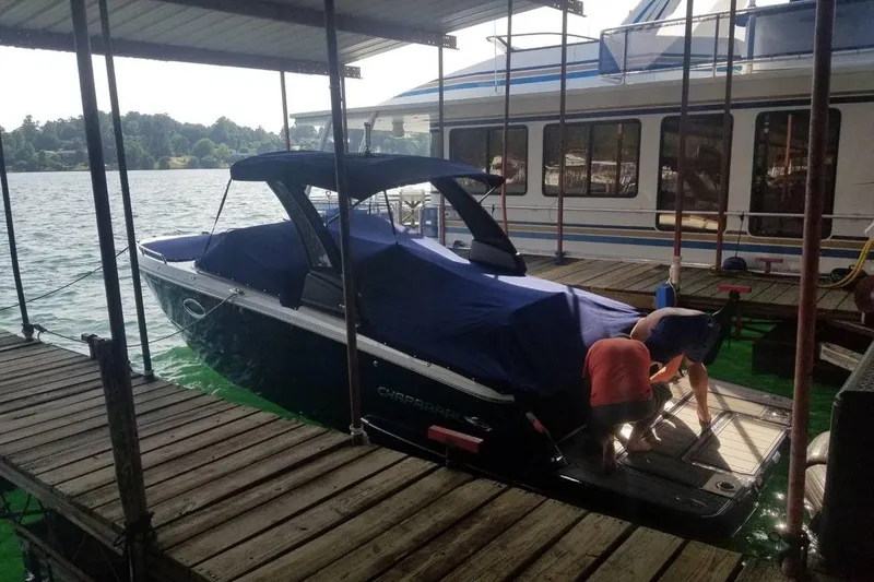 Slide: The Image of 2022 Chaparral 267 SSX boat docked, covered, with two people working nearby. - 4