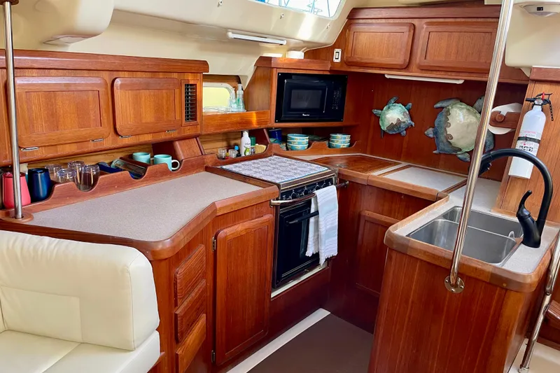 Slide: The Image of 1998 Hunter Passage 42 yacht kitchen with wooden cabinetry, stove, sink, and microwave. - 37