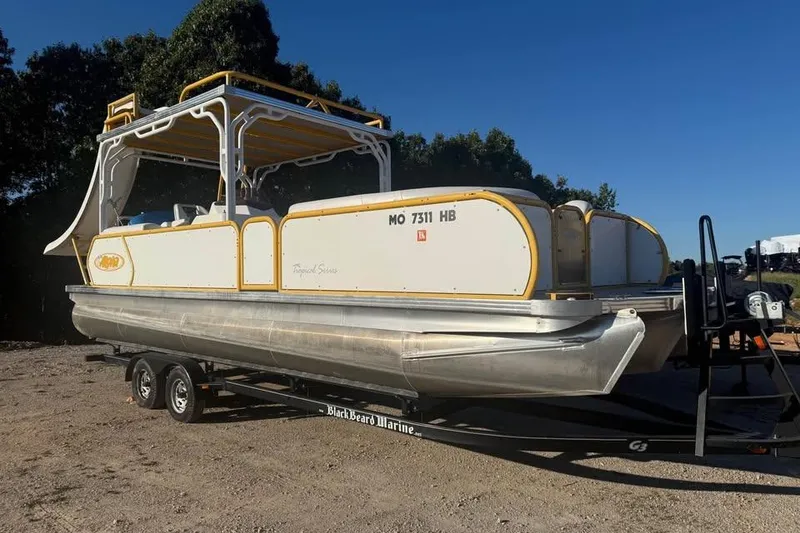 Slide: The Image of 2022 Aloha Pontoon Tropical 260 on trailer, parked outdoors under clear blue sky. - 1