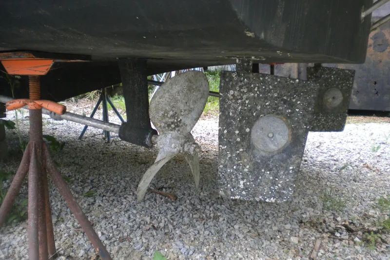 Slide: The Image of 1988 Mainship 40 Double Cabin boat propeller and rudder with barnacle growth on gravel. - 53