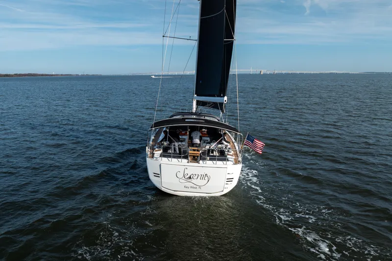 Slide: The Image of 2016 Jeanneau 64 yacht sailing on open water, rear view with American flag. - 14