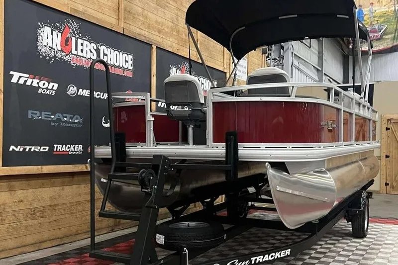 Slide: The Image of 2026 Sun Tracker Bass Buggy 18 DLX pontoon boat displayed indoors on a trailer. - 7