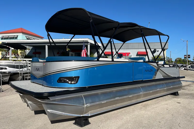 The Image of 2026 Avalon 2585 LSZ Entertainer Tri Toon boat with blue and silver design, parked outdoors. - 0