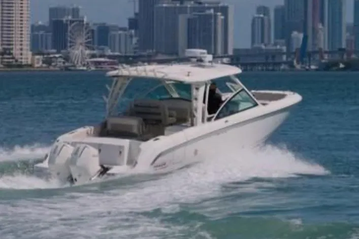 The Image of 2021 Boston Whaler 320 Vantage cruising on water with city skyline backdrop. - 0