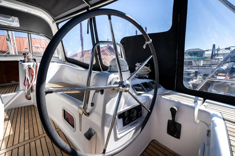 Slide: The Image of Steering wheel of 2013 Beneteau Oceanis 50 sailboat, featuring teak deck and navigation controls. - 51