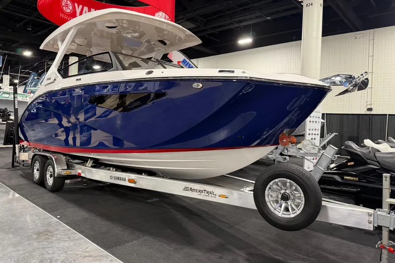Slide: The Image of 2026 Yamaha Boats 295SD on trailer, showcased indoors with sleek blue and white design. - 2