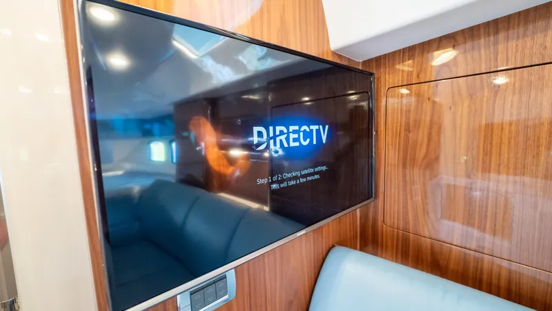 Slide: The Image of 2018 Intrepid 430 Sport Yacht interior with TV displaying DirecTV, featuring sleek wood paneling. - 38