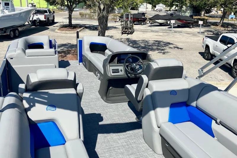 Slide: The Image of 2026 Sun Tracker Party Barge 22 DLX interior with gray and blue seating, parked outdoors. - 7