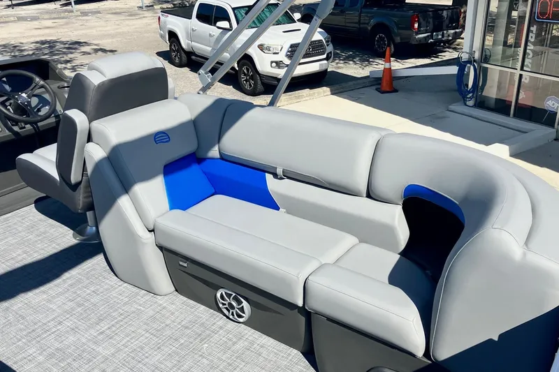 Slide: The Image of 2026 Sun Tracker Party Barge 22 DLX with gray and blue seating, parked outdoors. - 8