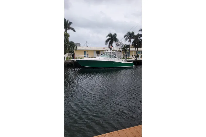 The Image of 2004 Cabo 40 Express yacht docked by palm trees on a cloudy day. - 0