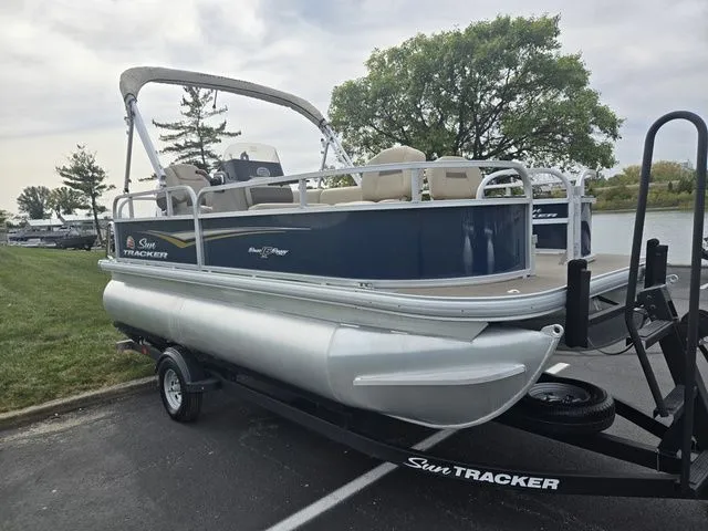 Slide: The Image of 2025 Sun Tracker Bass Buggy 16 XL Select pontoon boat on trailer, parked near a lake. - 9