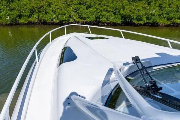 Slide: The Image of 2023 Intrepid 438 Evolution boat deck with railing, cruising near lush greenery. - 11
