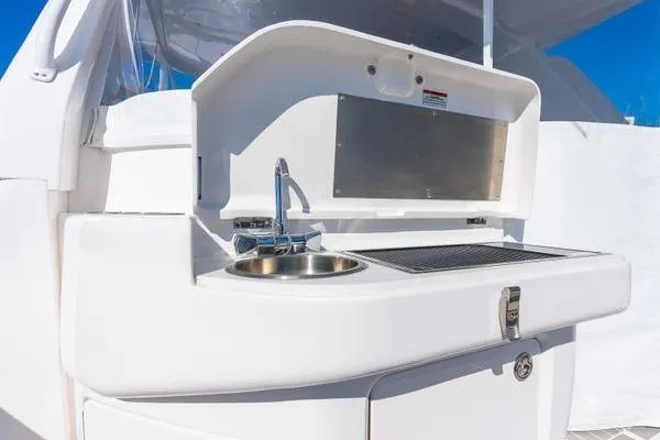 Slide: The Image of 2023 Intrepid 438 Evolution yacht kitchenette with sink and grill under blue sky. - 12