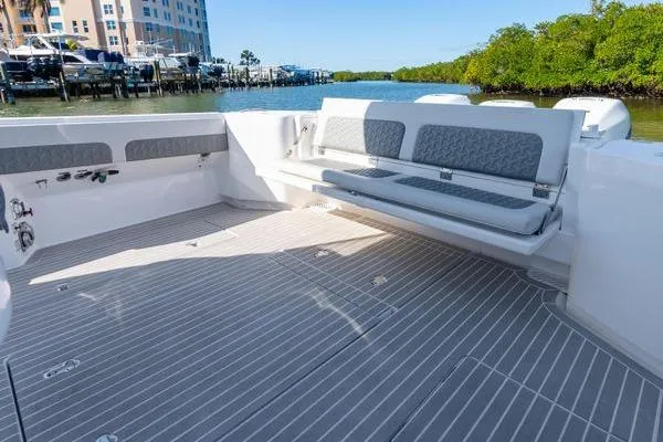 Slide: The Image of 2023 Intrepid 438 Evolution boat deck with seating, docked near lush greenery. - 15
