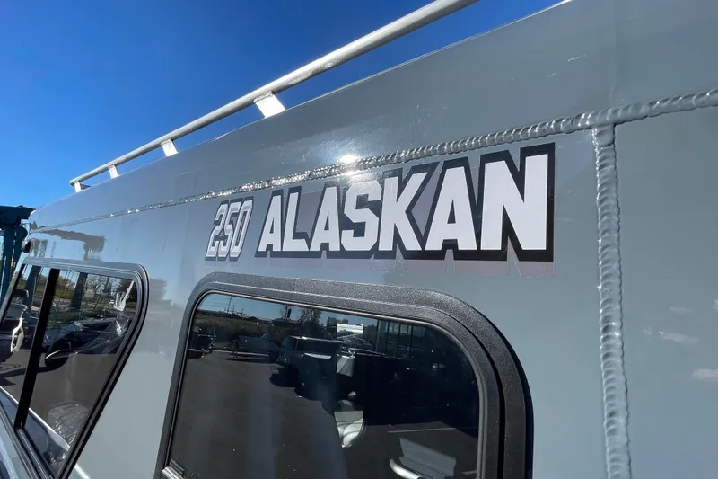 Slide: The Image of 2026 Hewescraft 250 Alaskan ET HT boat exterior with logo under clear blue sky. - 33