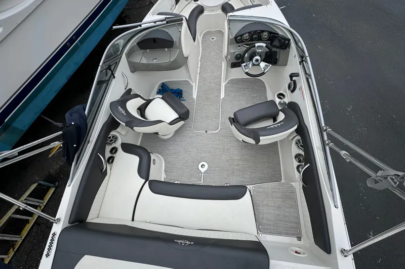 Slide: The Image of 2017 Stingray 204 LR boat interior with seating and steering wheel, docked beside another vessel. - 9