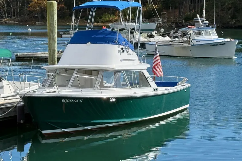 The Image of 1963 Bertram 31 Flybridge Cruiser docked, green hull, American flag, calm water. - 0