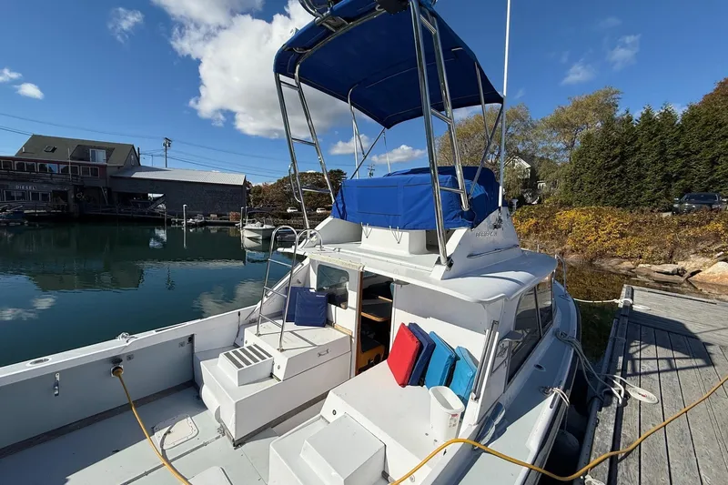 Slide: The Image of 1963 Bertram 31 Flybridge Cruiser docked by a serene waterfront under a blue sky. - 11