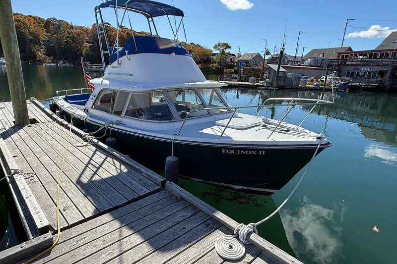 Slide: The Image of 1963 Bertram 31 Flybridge Cruiser docked, named Equinox II, in a serene marina setting. - 4