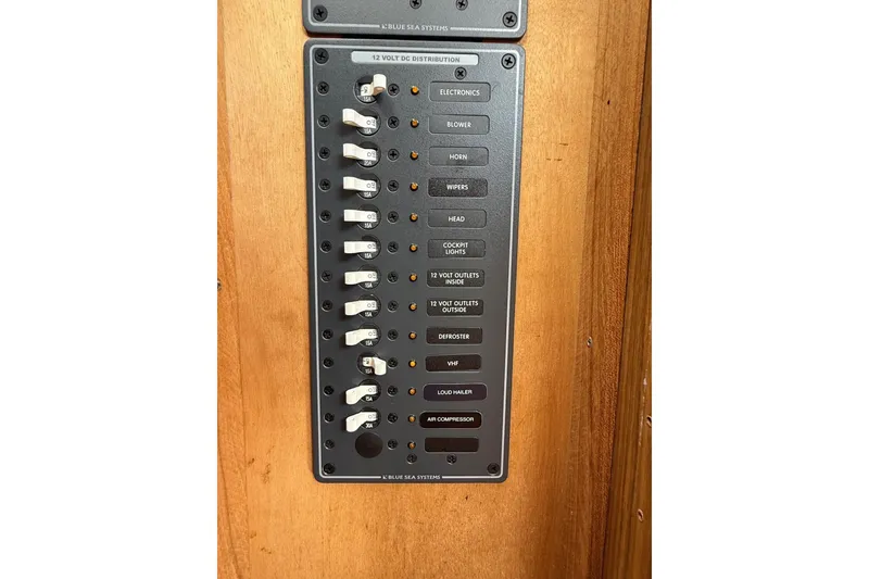Slide: The Image of 1963 Bertram 31 Flybridge Cruiser electrical panel with labeled switches on wooden background. - 42