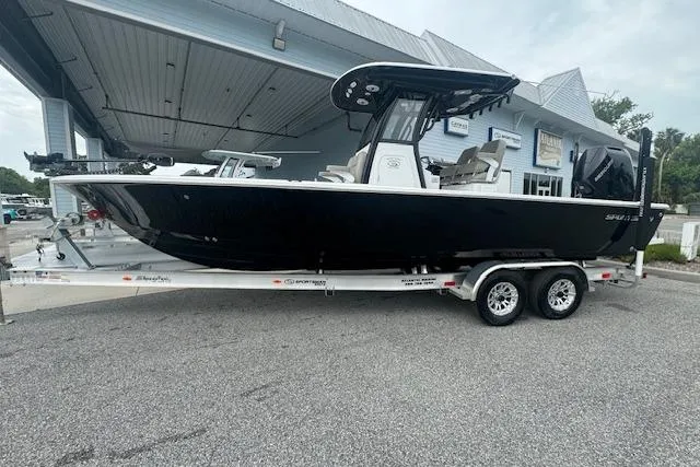 The Image of 2025 Sportsman Masters 267OE Bay Boat on trailer, sleek black design, parked outdoors. - 0