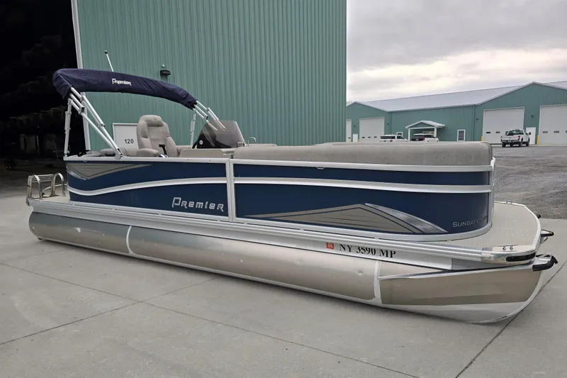 The Image of 2019 Premier 240 SunSation pontoon boat with blue and silver design, parked near green buildings. - 0