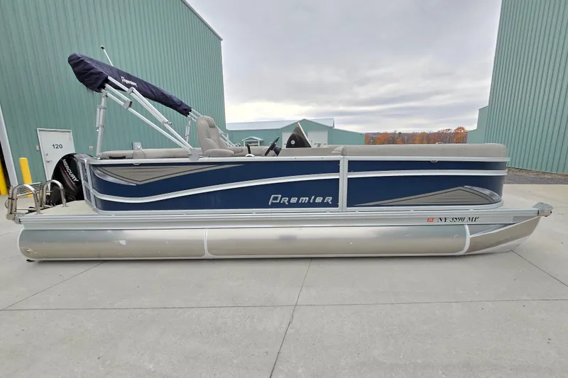 Slide: The Image of 2019 Premier 240 SunSation pontoon boat with blue and silver design, parked outdoors. - 2