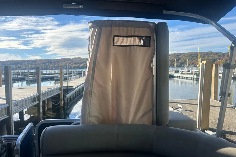 Slide: The Image of 2019 Premier 240 SunSation pontoon boat with gray seating and privacy curtain, docked near green buildings. - 21